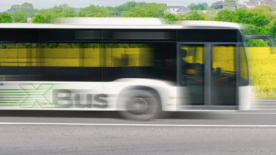 XBus von der Seite vor einem Rapsfeld in Bewegungsunschärfe