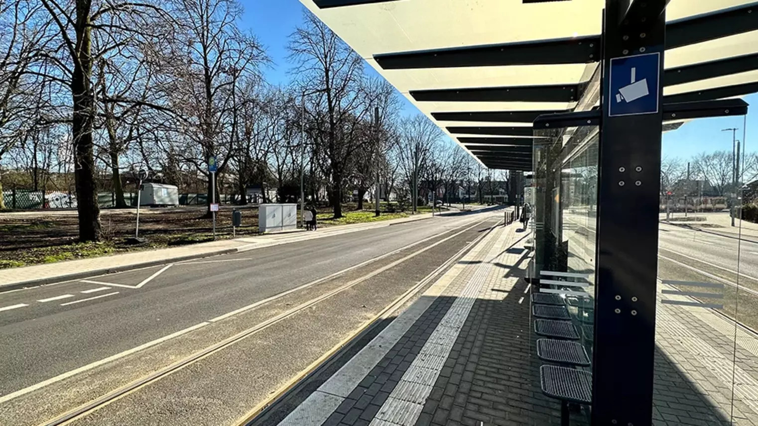 Neubau Haltestelle Brückelstraße: Blick auf die fertige Haltestelle mit Wetterschutz, Sitzgelegenheiten und einem Hinweisschild auf Videoüberwachung, im Hintergrund ist ein Fahrgast zu sehen