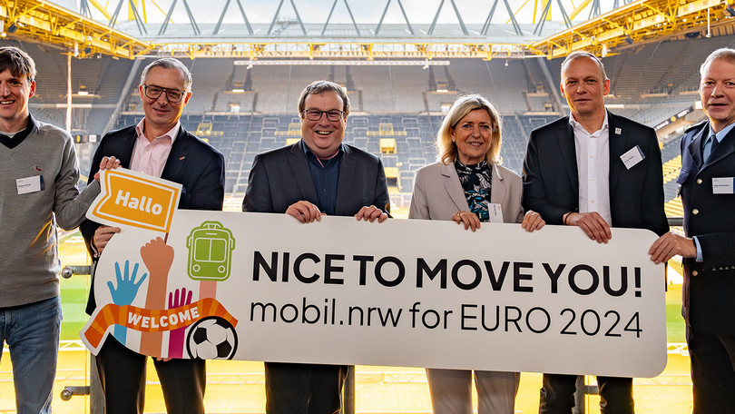 Eine Personengruppe um NRW-Verkehrsminister Oliver Krischer hält ein Schild mit der Aufschrift "Nice to move you! mobil.nrw for EURO 2024" hoch