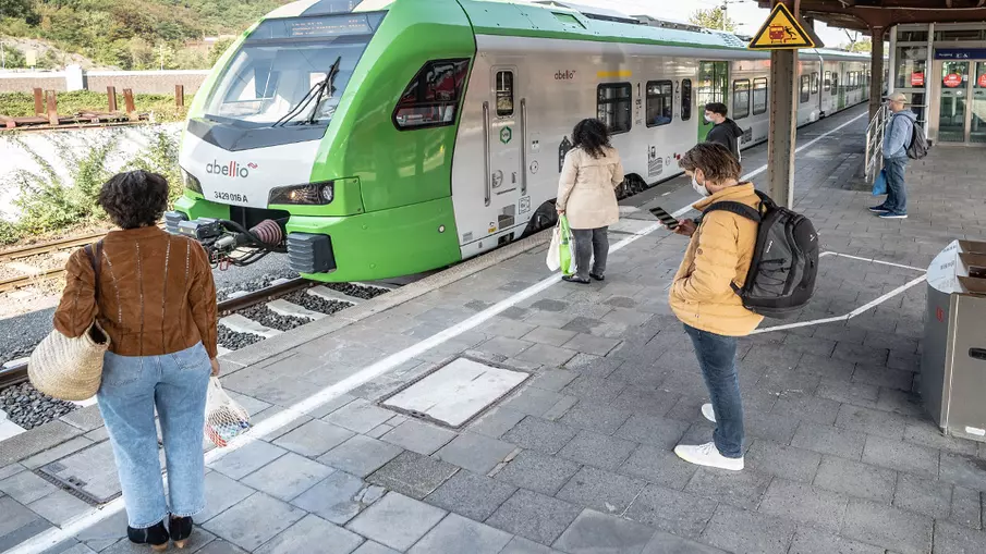 Blick auf einen Bahnsteig mit grüner S- Bahn im Hintergrund, wartende Fahrgäste vor dem Zug