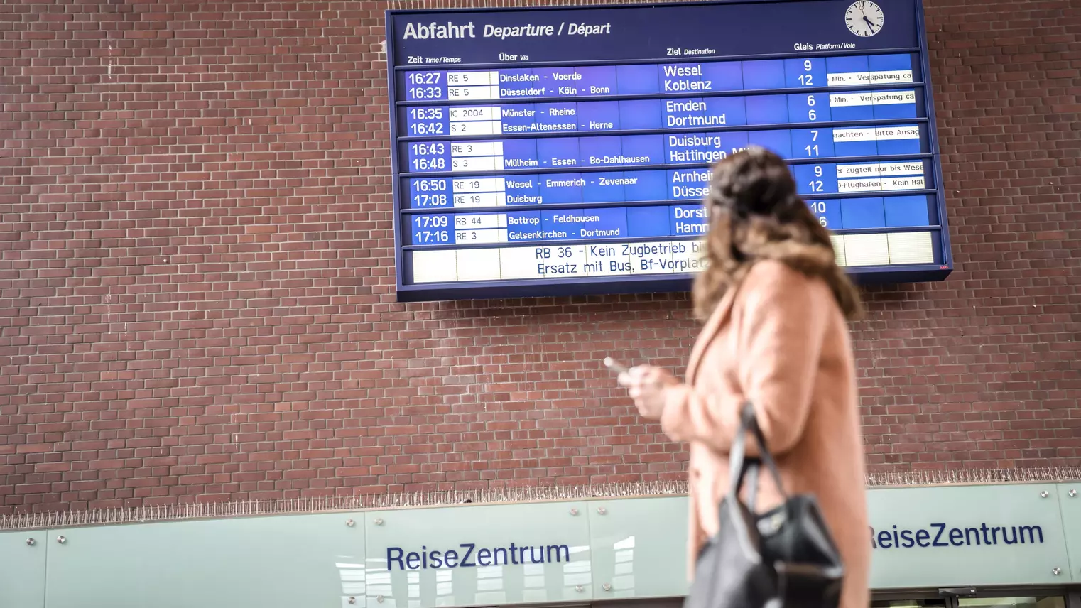 Eine Frau steht vor der Abfahrtsinfo-Tafel in der Bahnhofshalle