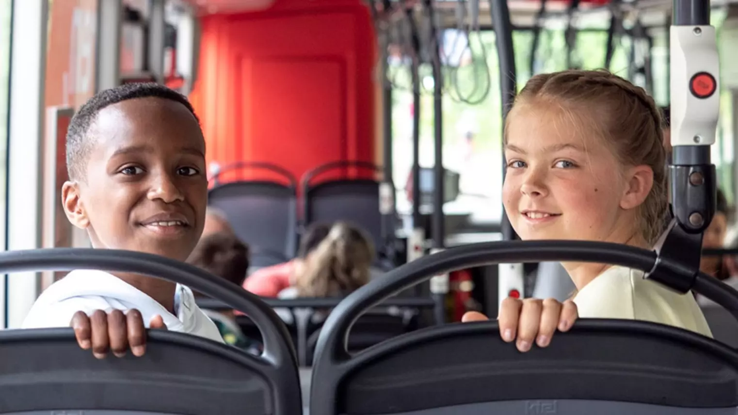 Ein Junge und ein Mädchen sitzen in einem Bus und schauen in die Kamera