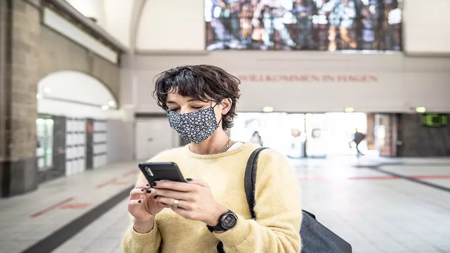 Eine Frau steht in einer Bahnhofshalle und blickt auf ihr Smartphone.