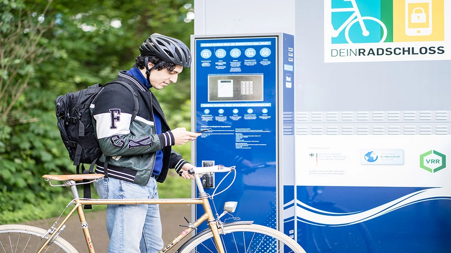 Ein Mann steht mit seinem Fahrrad vor einer DeinRadschloss-Station