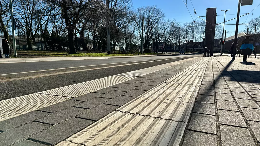 Neubau Haltestelle Brückelstraße: Detailaufnahme des fertigen Bahnsteigs mit taktilen Leitelementen, im Hintergrund sind Schienen und die Fahrbahn zu sehen