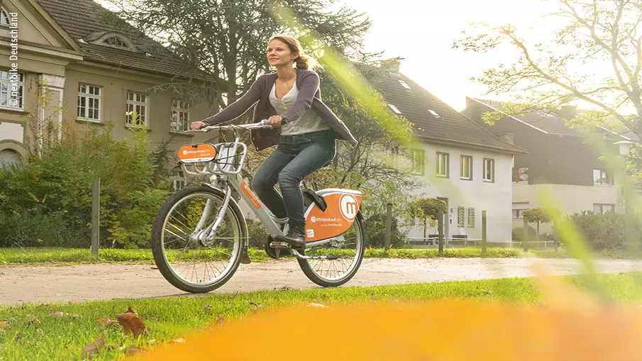 Eine Frau radelt mit einem Leihrad durch einen Park.