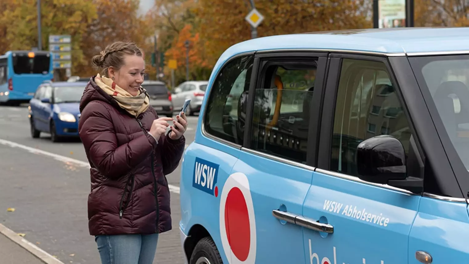 Eine junge Frau steht vor einem "WSW Cabs"-Fahrzeug und tippt auf ihr Smartphone