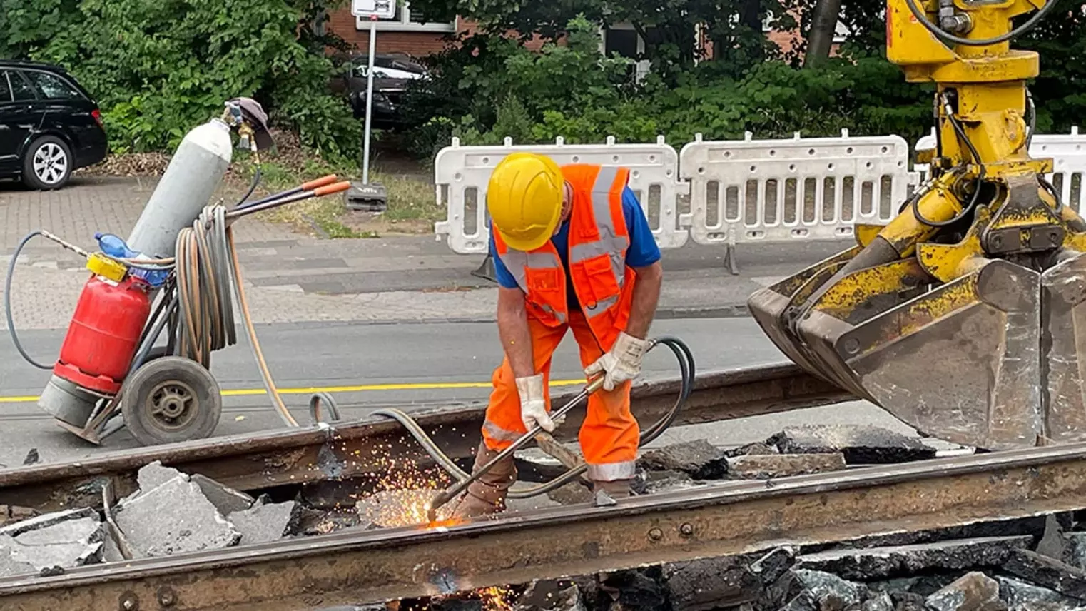 Neubau Haltestelle Brückelstraße: Eine Baumaschine hebt alte Gleise an, ein Bauarbeiter verrichtet Schweißarbeiten