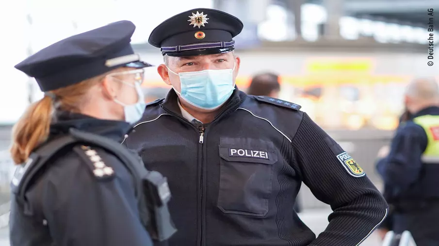 Zwei Bundespolizist*innen stehen am Bahnsteig, Sicherheitspersonal im Hintergrund