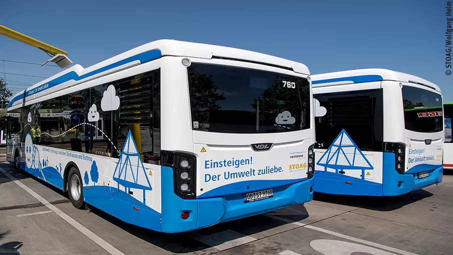 Zwei Elektrobusse der STOAG, über einem der Busse ist die Ladeinfrastruktur zu sehen