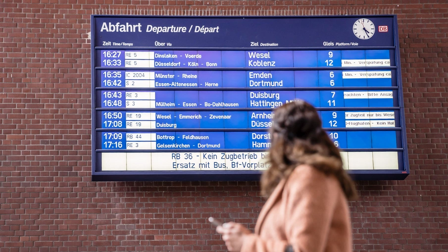 Blick auf eine Fahrgastinformationstafel in einem Bahnhof, im Vordergrund ist eine Person zu sehen, die auf die Tafel blickt