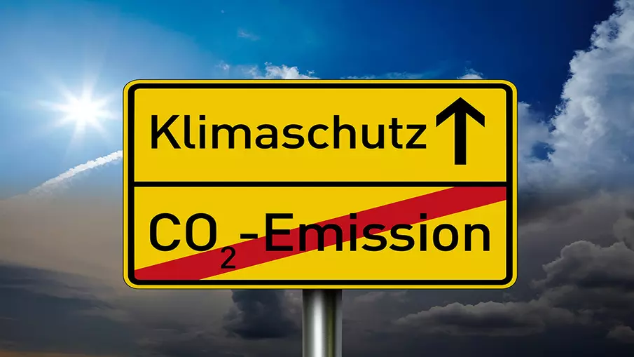 Gelbes Schild, unten ist rot durchgestrichen "CO2-Emission" zu lesen, oben mit einem Pfeil nach oben "Klimaschutz"