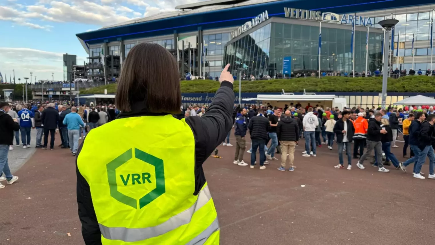 Eine Frau mit VRR-Weste zeigt auf die Veltins-Arena