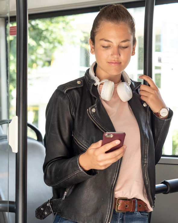 Eine junge Frau steht im Bus und schaut auf ihr Smartphone