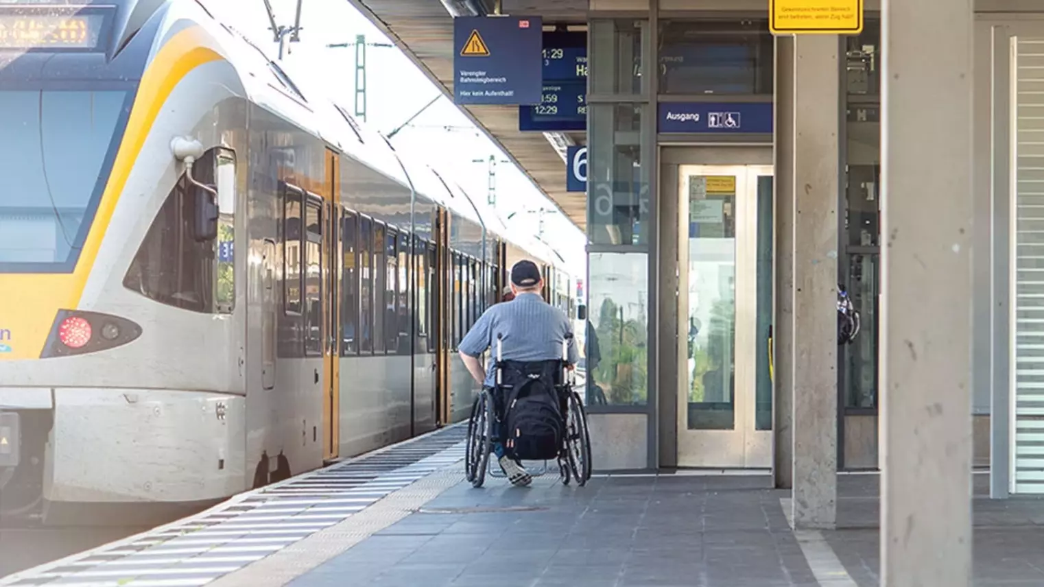 Ein Rollstuhlfahrer ist am Bahnsteig unterwegs zum stehenden Zug