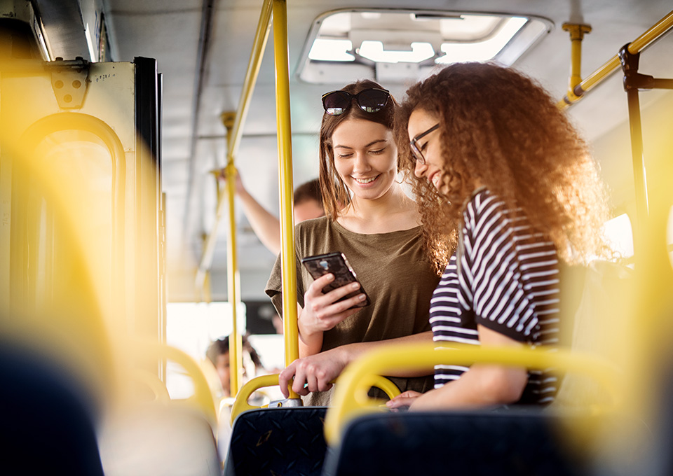 Zwei Frauen stehen im Bus und blicken auf ein Smartphone