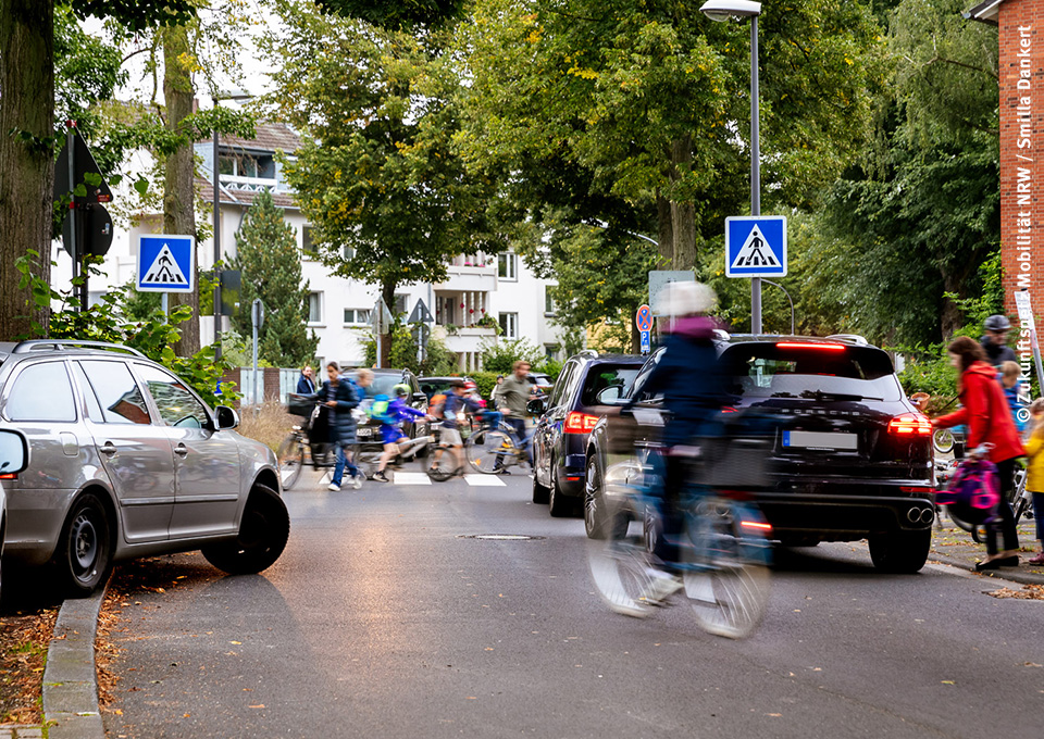 Reger Verkehr an einem Zebrastreifen: Fußgänger und Fahrradfahrer treffen auf Autos