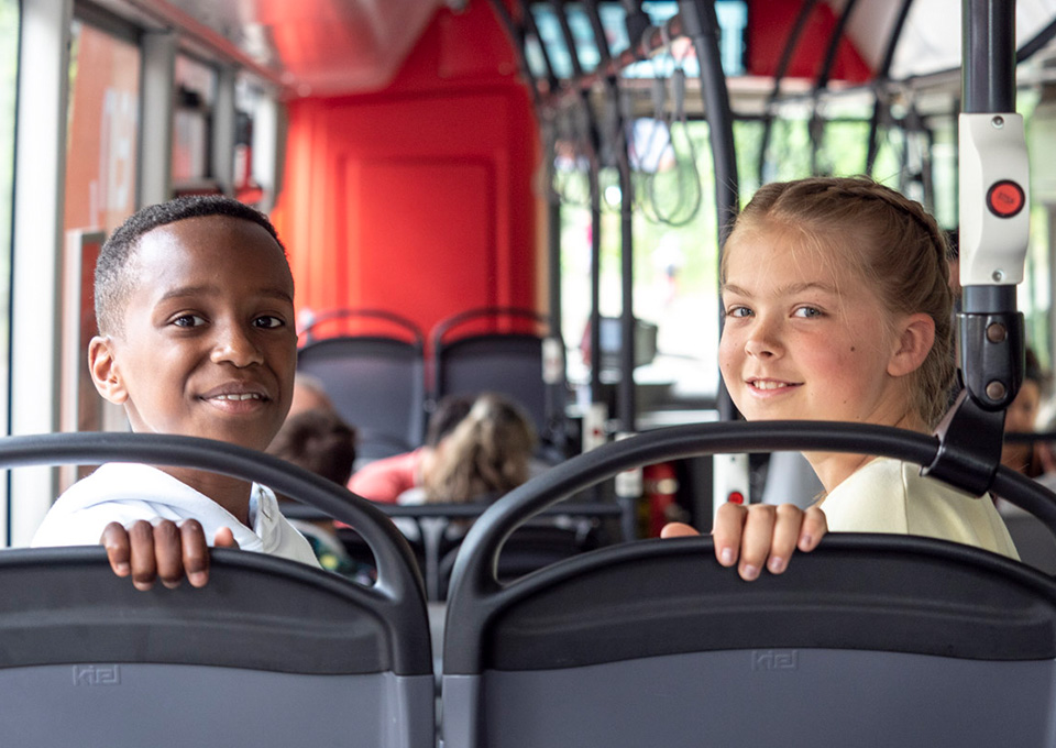 Ein Junge und ein Mädchen sitzen in einem Bus und schauen in die Kamera