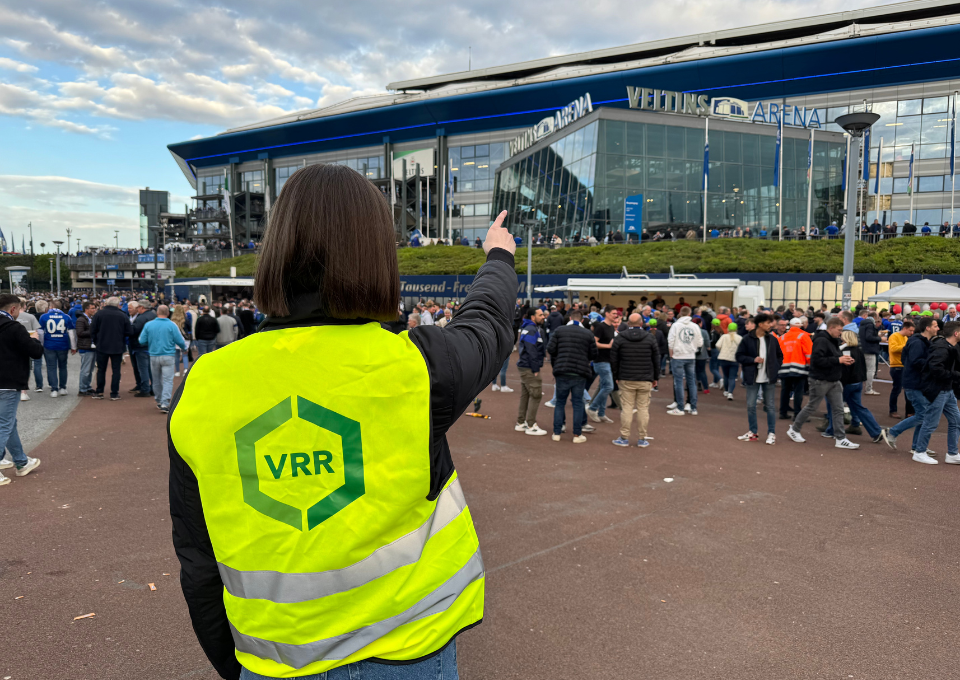 Eine Frau mit VRR-Weste zeigt auf die Veltins-Arena