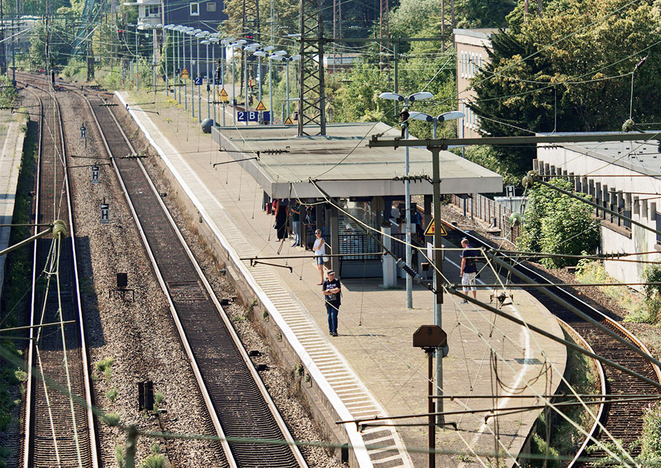 Blick auf einen Bahnhof mit Bahnsteig und Gleisen, am Bahnsteig stehen Reisende